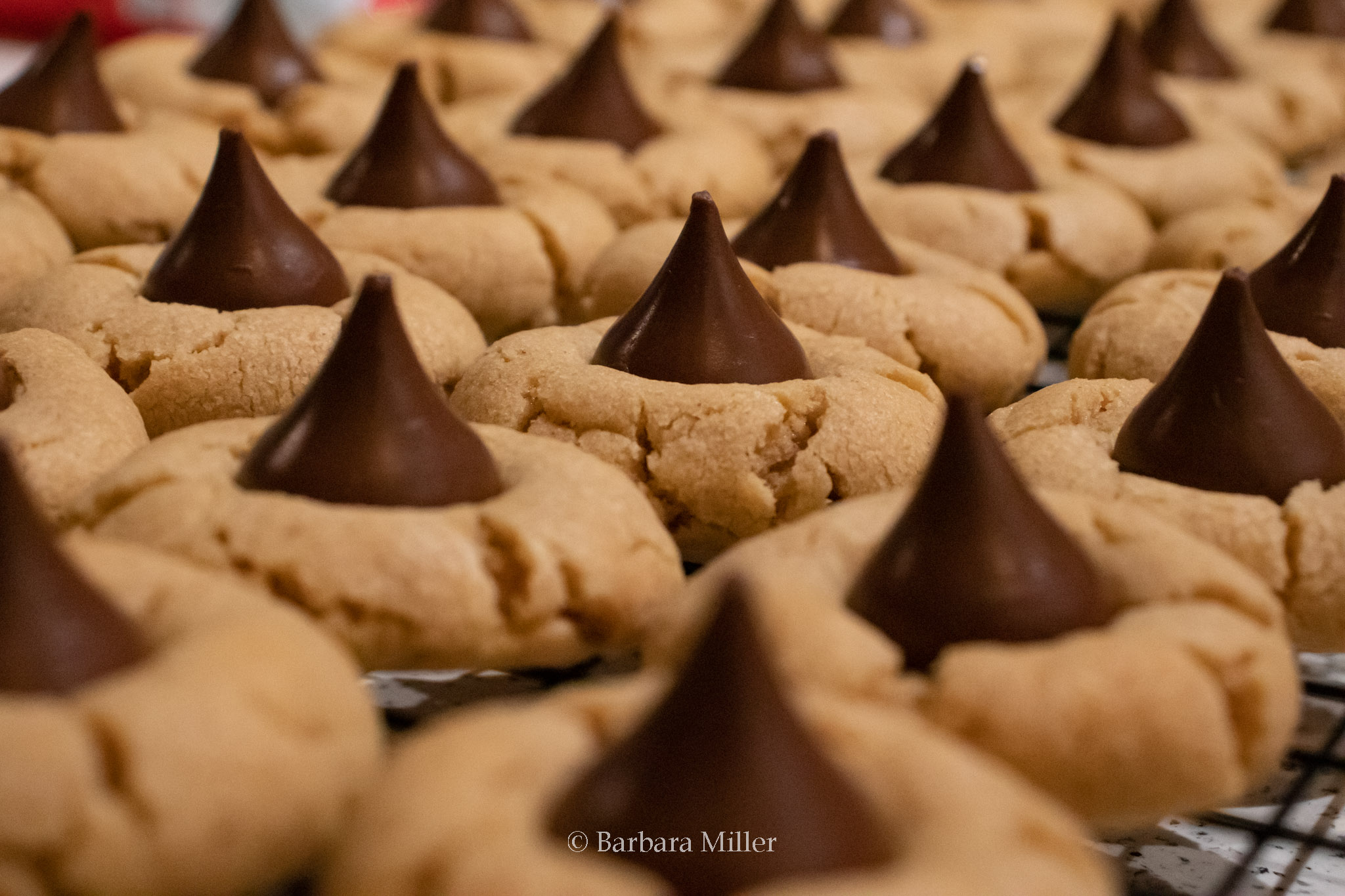 Several rows of peanut butter cookies with Hershey kisses on top.